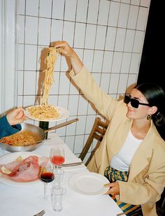 two people sitting at a table with plates of food in front of them and one person holding up a plate