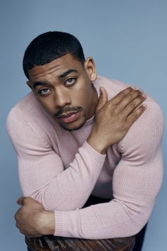 a man in a pink sweater is leaning on a wooden chair with his arms crossed