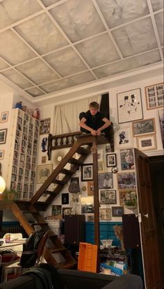 a boy is standing on the top of a ladder in his room with pictures all around him