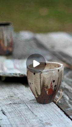 two cups sitting next to each other on top of a wooden table with paint splattered