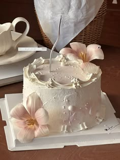 a white cake with pink flowers on it and a tea cup next to it in the shape of a heart