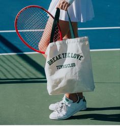 a woman holding a tennis racquet and a tote bag on a court