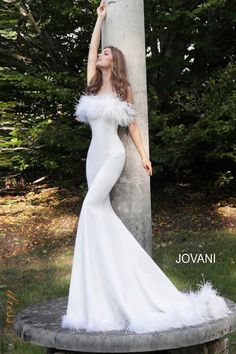 a woman in a long white dress leaning against a tree trunk and posing for the camera