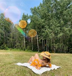 a woman laying on top of a blanket in the grass with balloons flying above her