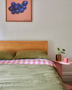 a bed with green sheets and pillows in a bedroom next to a painting on the wall