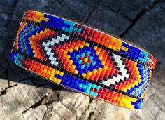 a colorful beaded bracelet sitting on top of a piece of wood next to a rock