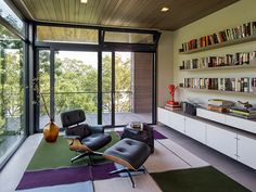 a living room with chairs, bookshelves and a large glass door leading to the outside