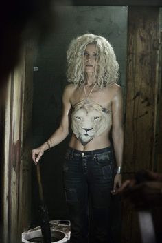 a woman standing next to a toilet with a lion on it's chest and an ax in her hand