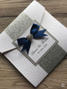 a wedding card with a blue ribbon on top and silver glitters around the edges