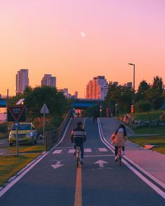 two bicyclists are riding down the road at sunset with city in background