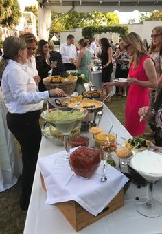 a group of people standing around a table filled with plates and bowls full of food