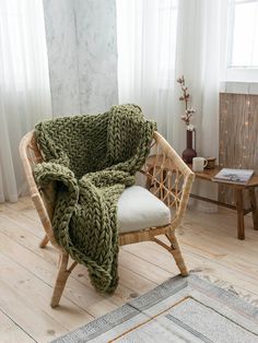 a chair with a blanket on top of it in front of a wooden table and window