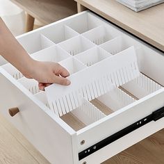 a person holding a drawer open with several compartments in it on top of a wooden table