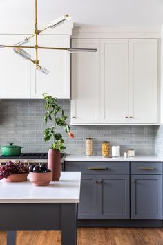 a kitchen with white cabinets and gray counter tops, plants in pots on the island