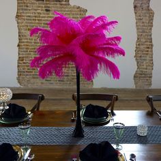 there is a table set with place settings and a pink feather centerpiece on it