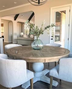 a dining room table with white chairs and flowers in a vase on the centerpiece