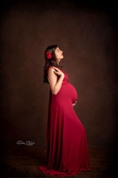 a pregnant woman in a red dress poses for the camera with her hands on her belly