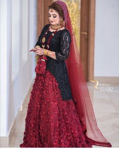 a woman in a red and black wedding dress standing next to a white wall wearing a veil