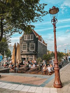 people are sitting at tables in front of a building on the waterfront with umbrellas