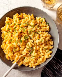 a bowl filled with macaroni and cheese on top of a table next to glasses