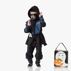 a little boy dressed in black and wearing a halloween costume with a trick bag next to him