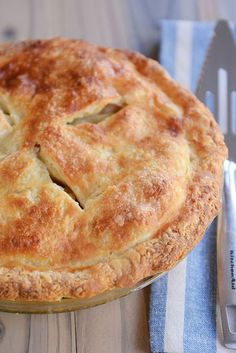 a pie sitting on top of a wooden table next to a knife and fork in front of it