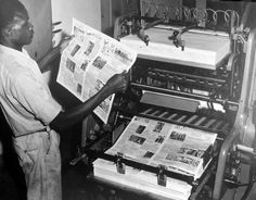 a man reading a newspaper while standing next to a machine with newspapers on top of it