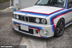 the front end of a white bmw car with blue, red and black stripes on it