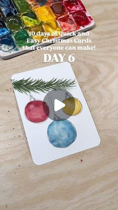 a wooden table topped with watercolors and a christmas ornament on it