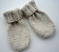 two white knitted mittens sitting on top of a table next to each other