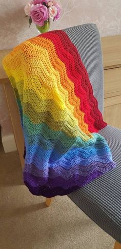 a crocheted rainbow blanket sitting on top of a chair next to a vase with flowers