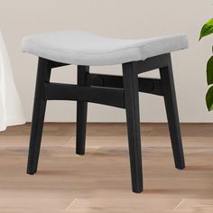 a grey upholstered stool sits in front of a potted plant on the floor