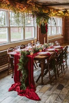 a long table with red cloth and greenery is set for an elegant christmas dinner