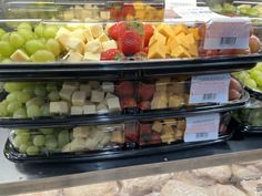 several trays filled with different types of fruits and cheese on display in a store