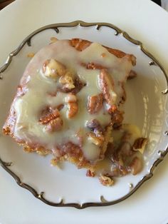 a white plate topped with a piece of cake covered in icing and nuts on top of it