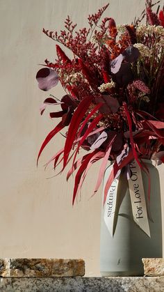 a vase filled with lots of flowers on top of a stone table next to a wall