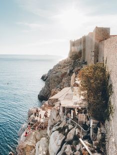 some people are swimming in the water near an old castle on top of a cliff