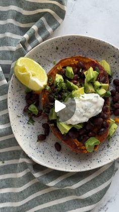 a white plate topped with black beans, avocado and sour cream on top