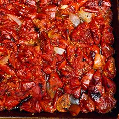 a pan filled with lots of red food on top of a wooden table next to utensils