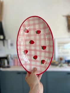 a person holding up a pink and white plate with strawberries painted on the side