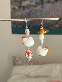 two earrings hanging from a clothes line in front of a bed with a painting on the wall behind them