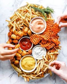 two hands reaching for dipping sauce on top of a plate of fries and dips