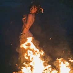 a woman standing in front of a fire with her back to the camera and arms behind her head