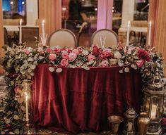 a table with flowers and candles on it in front of a red cloth covered table