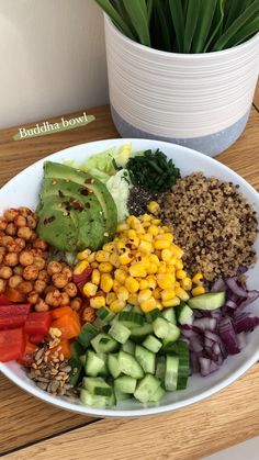 a white bowl filled with different types of vegetables and nuts next to a potted plant