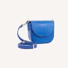 Diana is a new design of a saddle bag: Lizard leather, BLUE, glazed, silver finish. Cross body bag model. Our modern interpretation of a saddle bag. Hold all of your daily essentials in our sweet Diana crossbody. The refined shape and understated elegance makes this silhouette your perfect companion for all occasions. You can carry Diana as a shoulder bag or wear it more casually across the body. The sleek metallic chain with a luxurious leather shoulder guard add to the functionality of this versatile style. Blue Jean Purses, Shoulder Guard, Python Bags, Jean Purse, Pink Clutch, Crocodile Bags, Leather Saddle Bags, Burgundy Top, Bag Model