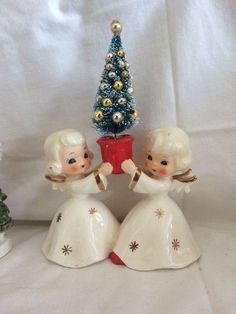 two figurines are next to a small christmas tree