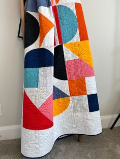 a woman standing next to a white wall with a quilt on it