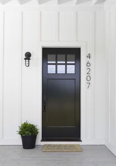 a black front door on a white house with a potted plant next to it