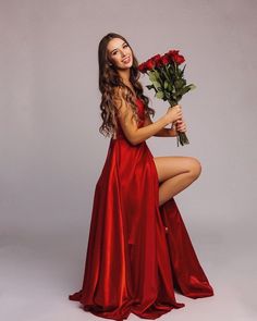 a beautiful young woman in a red dress holding flowers and posing with her legs crossed